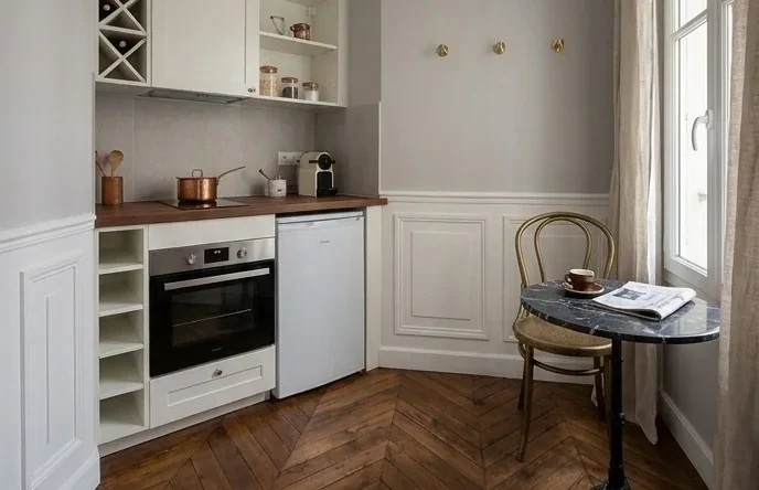 Cuisine ouverte sur le coin repas — façades laquées ivoire, plan de travail noyer, parquet à chevrons conservé